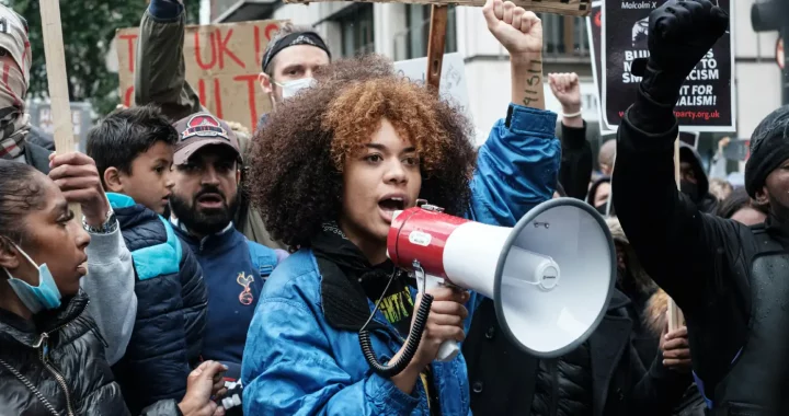 a young woman in focus holding a megaphone in the middle of a protest crowd
