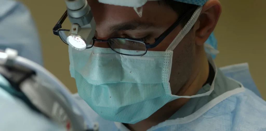 a zoom-in photo of a doctor wearing scrubs and a mask in the middle of a surgery