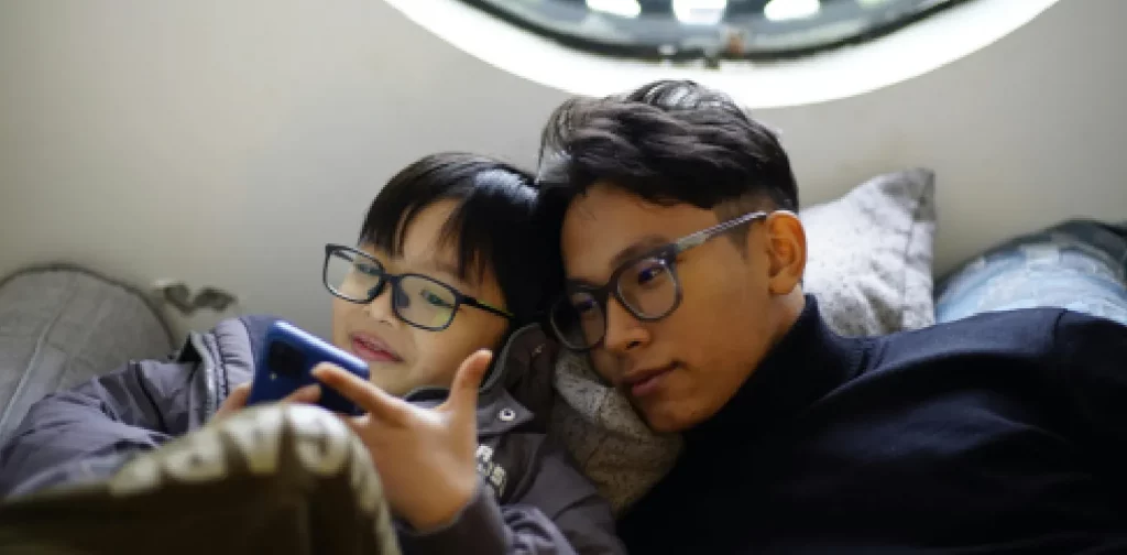 a boy and a man looking at a phone while wearing glasses
