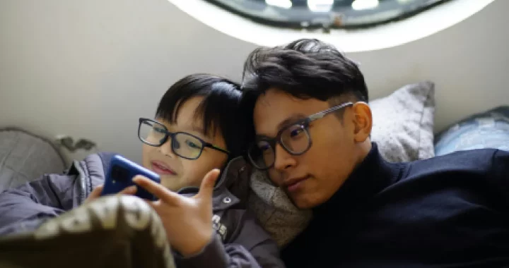 a boy and a man looking at a phone while wearing glasses