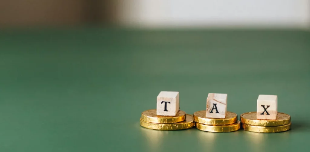 block letters forming the word ‘tax’ sitting on top of gold coins