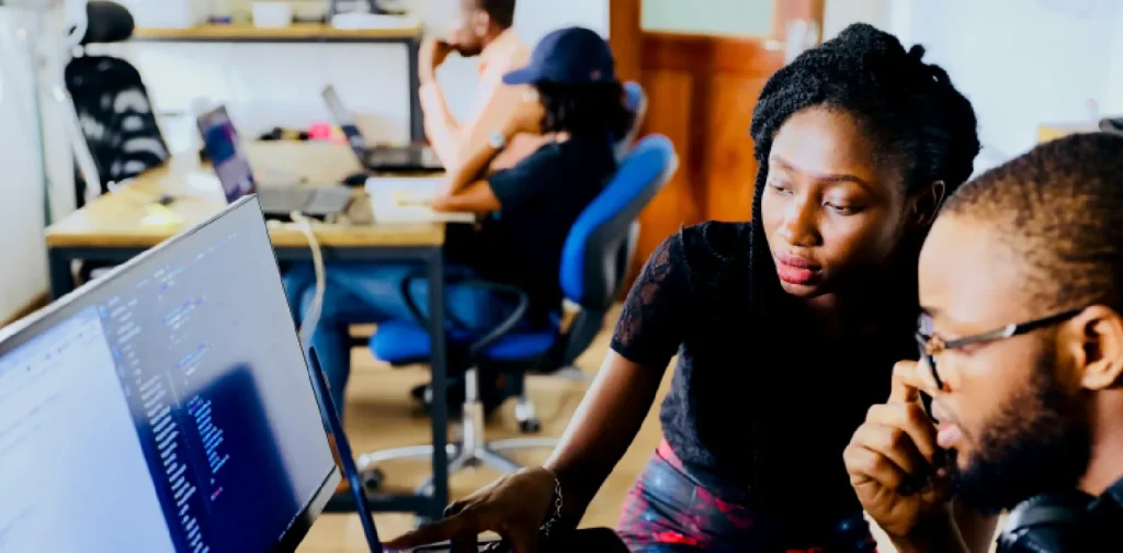 a young woman and man working in front of a monitor and a laptop