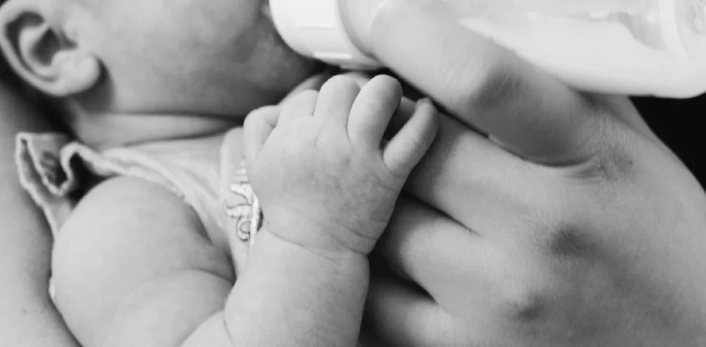 a grayscale photo of a baby being bottle-fed