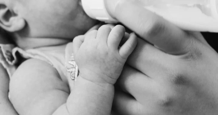 a grayscale photo of a baby being bottle-fed