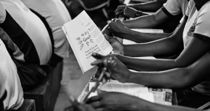 a grayscale photo of student sitting side by side in a classroom, holding a book