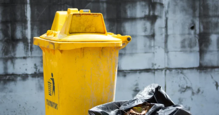 a yellow garbage bin with a plastic bag full of trash next to it