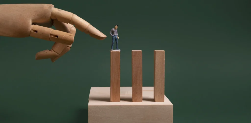 a small wooden figure of a man standing on a wooden block with a hand threatening to push him