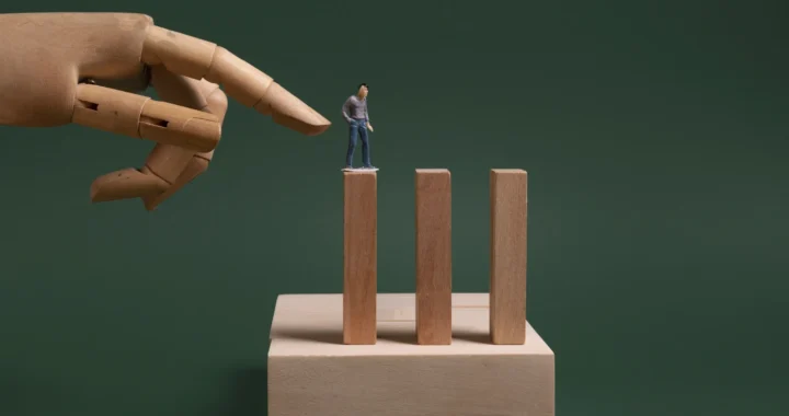 a small wooden figure of a man standing on a wooden block with a hand threatening to push him