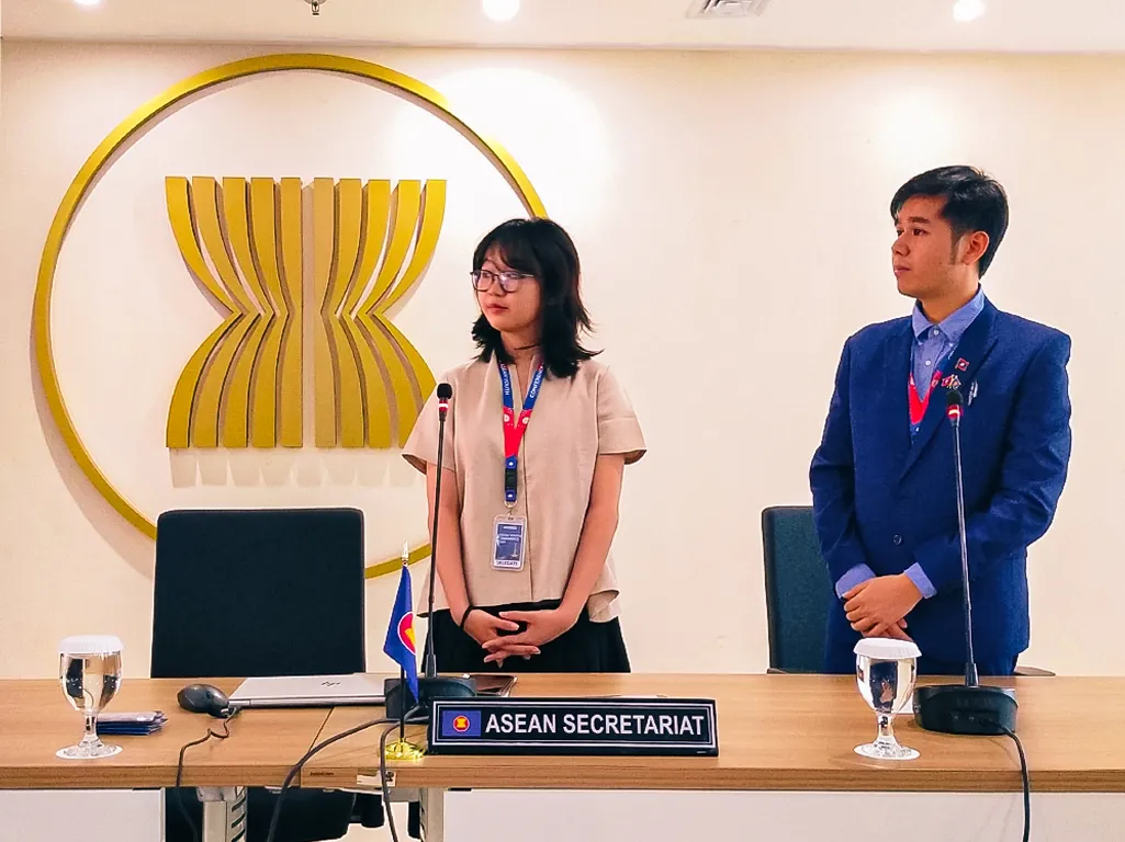 a young woman and a young man standing and presenting in front of the ASEAN logo