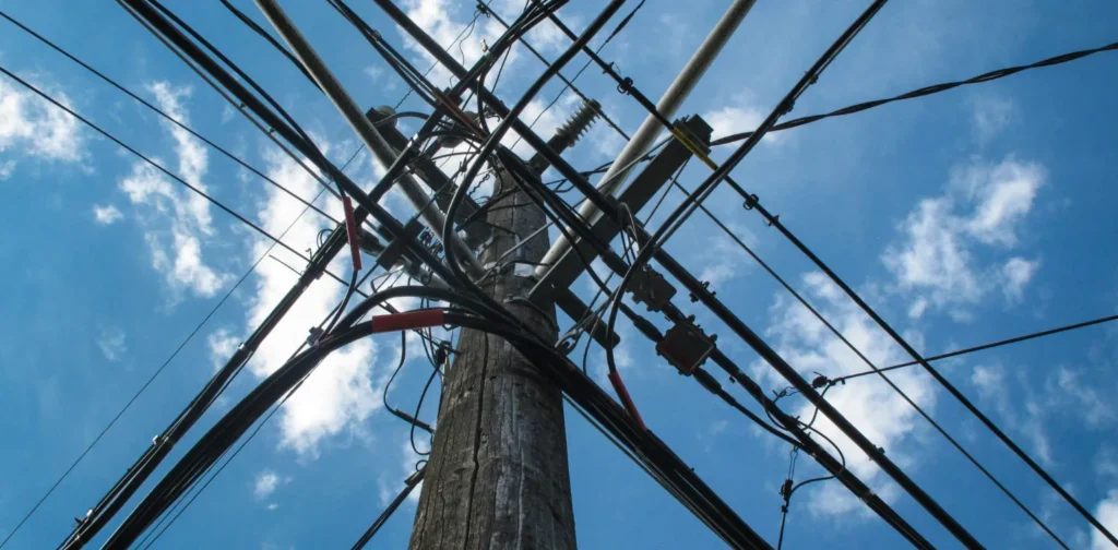 a low angle photo of electric post with a bunch of cables