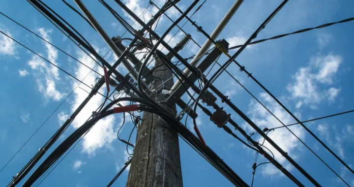 a low angle photo of electric post with a bunch of cables