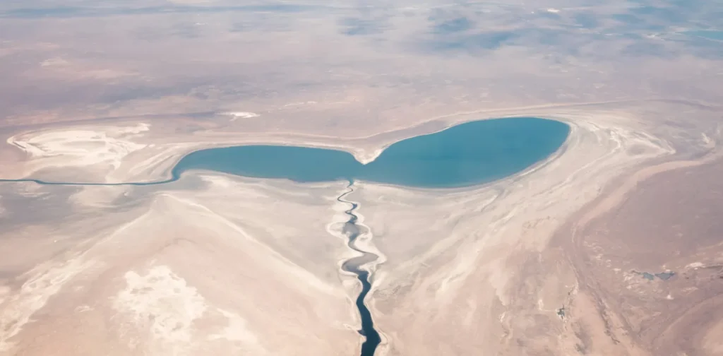 an aerial photo of Aral Sea, a quite large body of water in the middle of a dessert, connecting to a long river