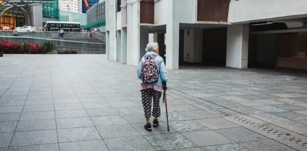 an elderly woman walking on a street with a walking stick, her back facing the camera