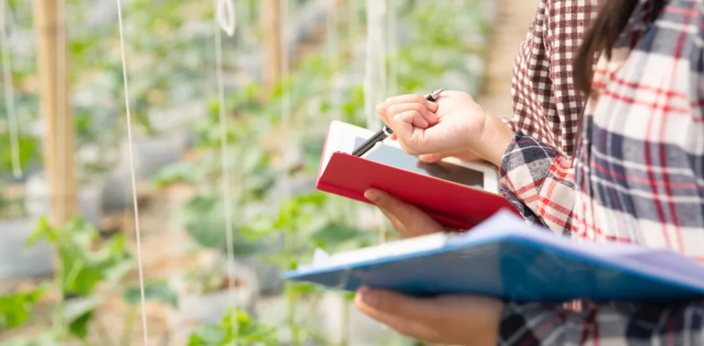 two people standing in front of a garden holding a tablet and papers