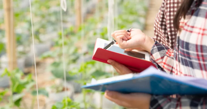 two people standing in front of a garden holding a tablet and papers