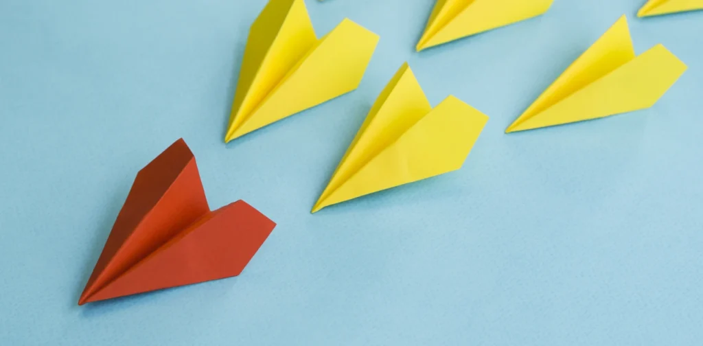 red paper plane leading yellow paper planes