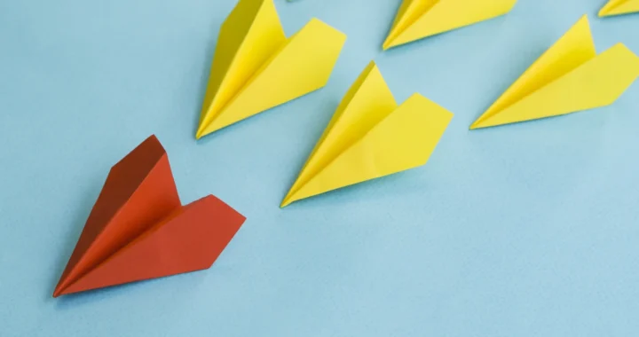red paper plane leading yellow paper planes