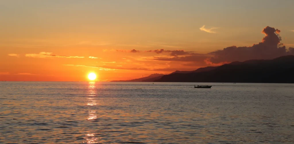 a silhouette of fishermen boat with sunset as the background