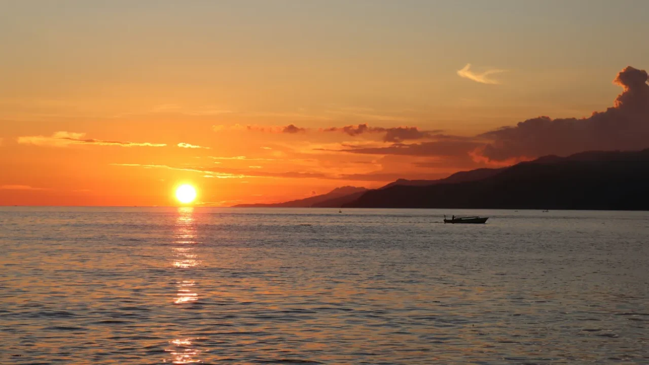 a silhouette of fishermen boat with sunset as the background