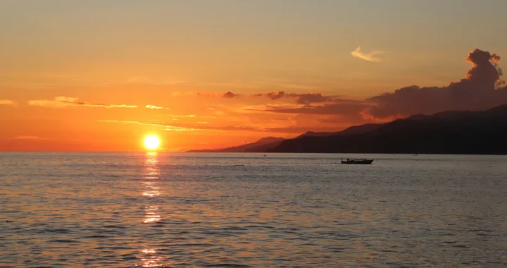 a silhouette of fishermen boat with sunset as the background