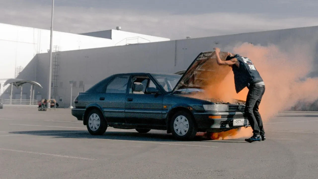 A man with a parked car with the hood open and smoke coming out