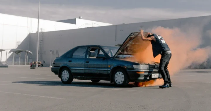 A man with a parked car with the hood open and smoke coming out