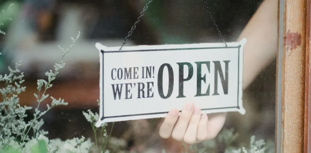 a hand holding on an open sign attached on a glass door