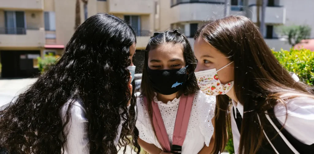 three girls wearing masks with their heads close together