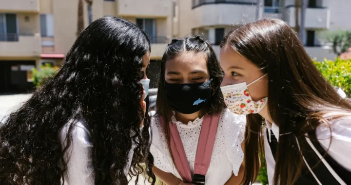 three girls wearing masks with their heads close together