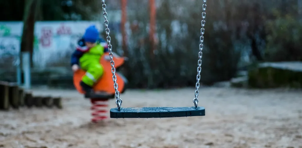 an empty swing with a child playing on the background