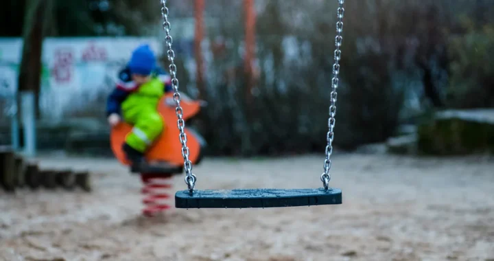 an empty swing with a child playing on the background