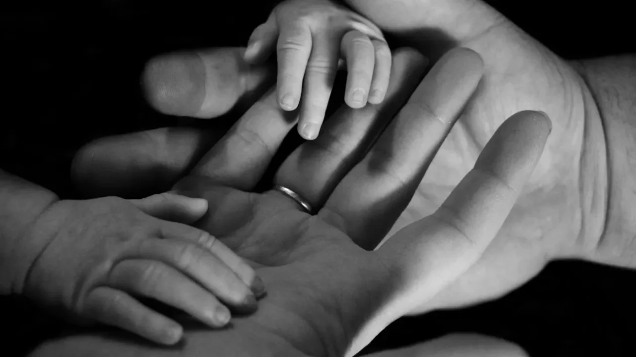 a grayscale photo of parent and baby hands