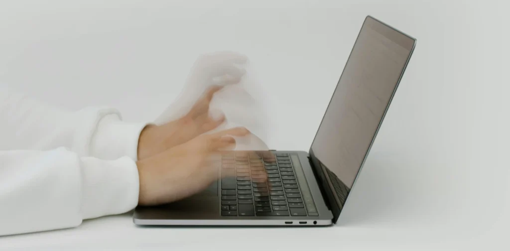 side view of motion blurred hands typing on a laptop.