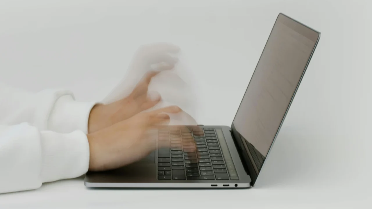side view of motion blurred hands typing on a laptop.