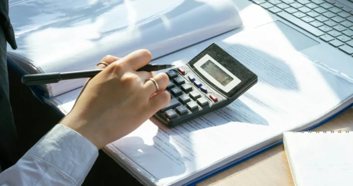 hands of a person trying to an esg report using a calculator on top of documents in front of a laptop