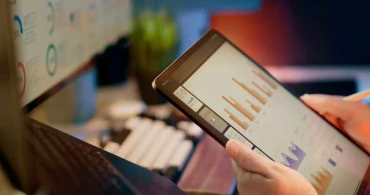 Someone analyzes financial data on a tablet and a monitor