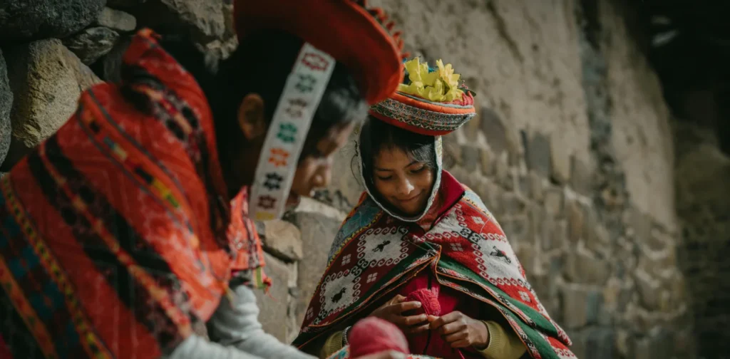two girls wearing traditional clothes of Peru sitting by a wall