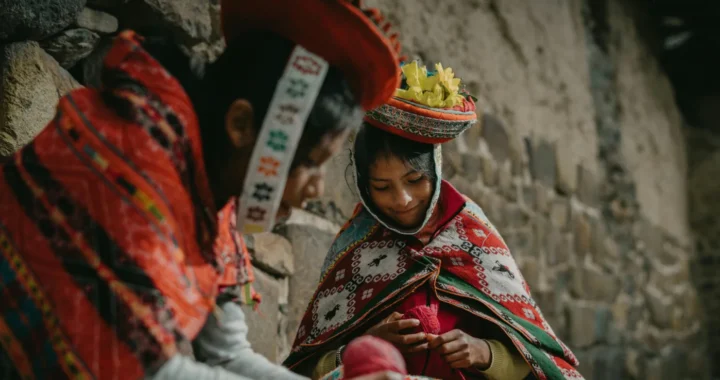 two girls wearing traditional clothes of Peru sitting by a wall