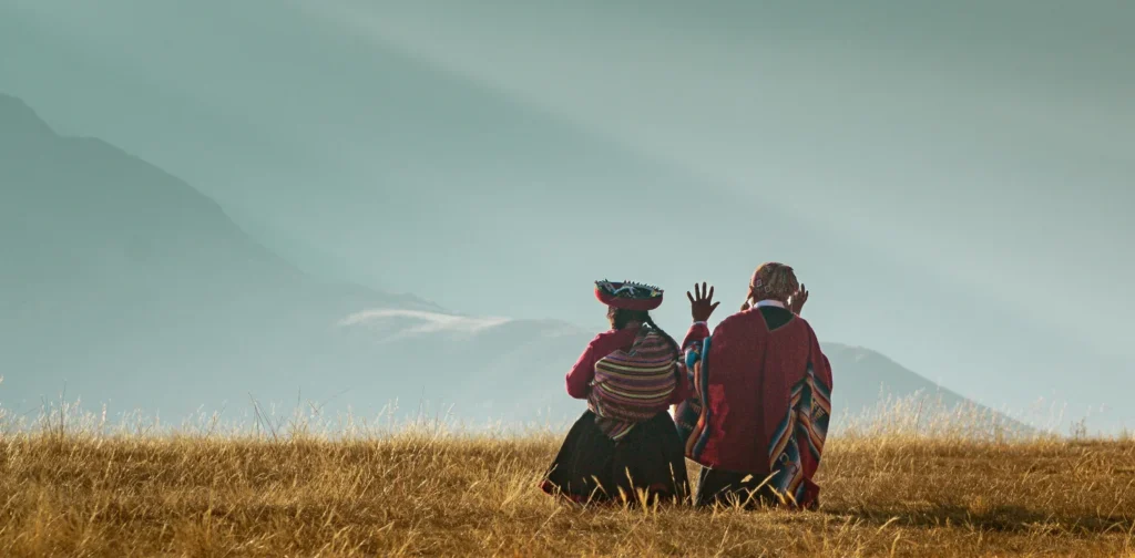 back view of two quechua women sitting on a grassy hill with mountains in the background