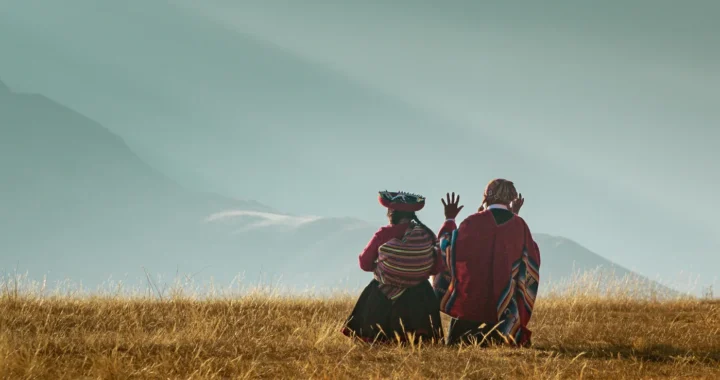 back view of two quechua women sitting on a grassy hill with mountains in the background