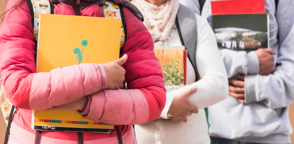 Close-up photo of three children holding notebooks and carrying backpacks