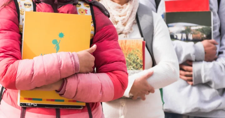 Close-up photo of three children holding notebooks and carrying backpacks