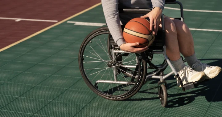 A disabled person in a wheelchair holding a basketball on the court.