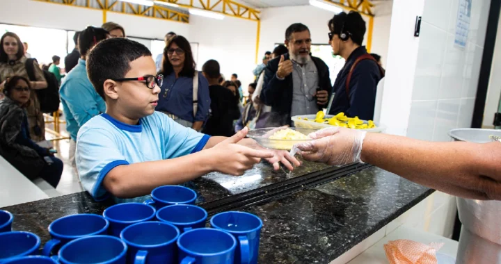 A child with glasses receives a tray of school meal.