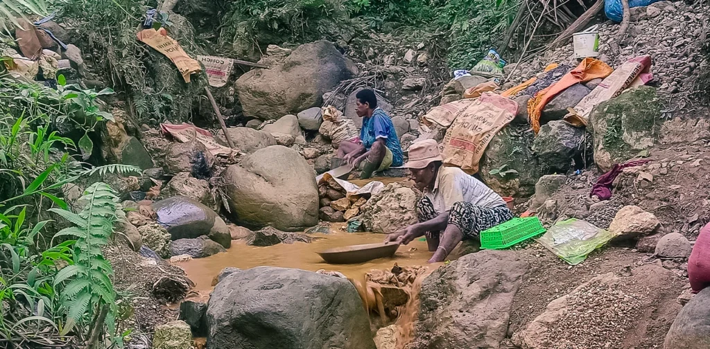 two women separating gold from sand using a pan