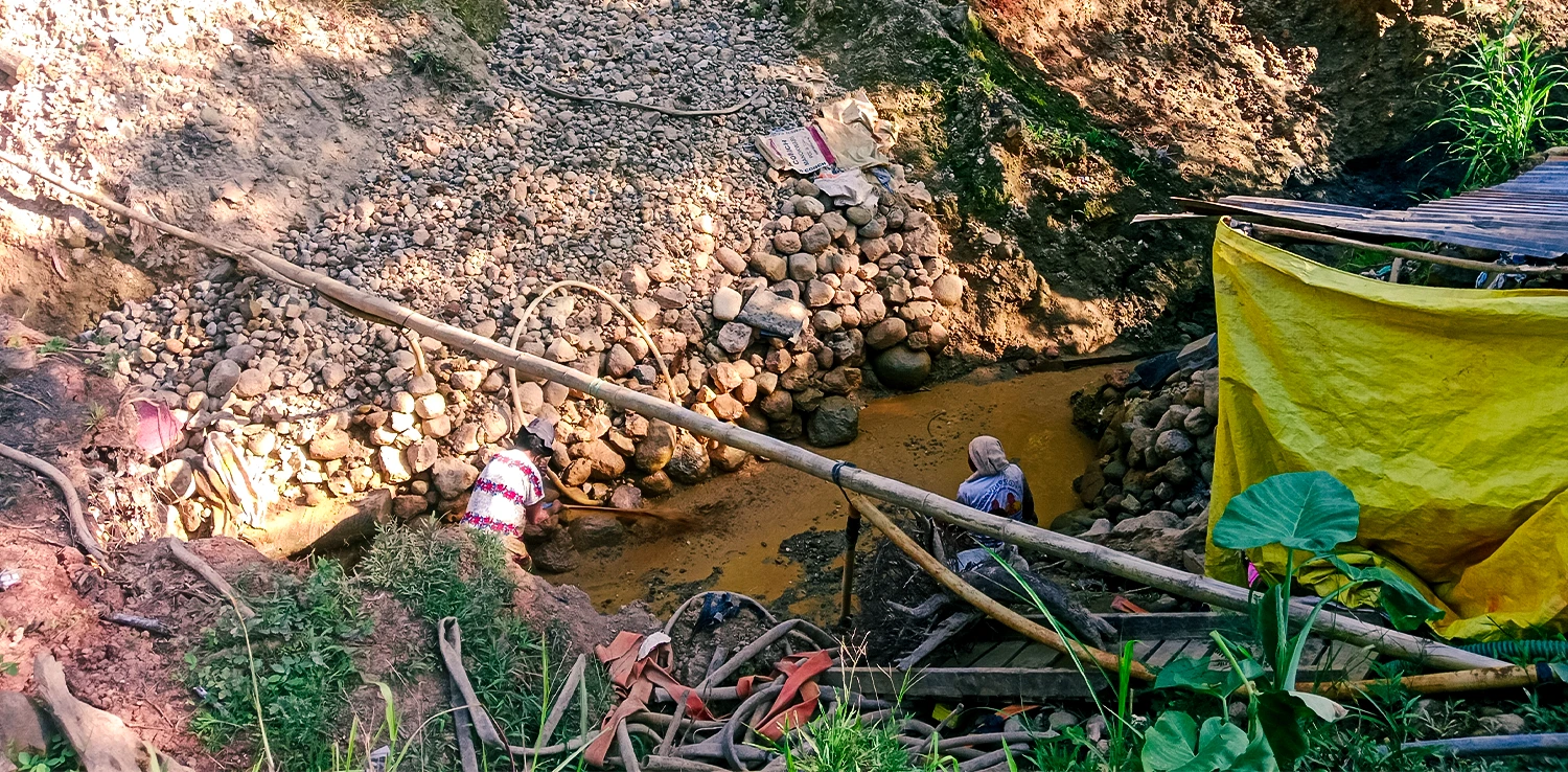 two people under a muddy soil excavation.