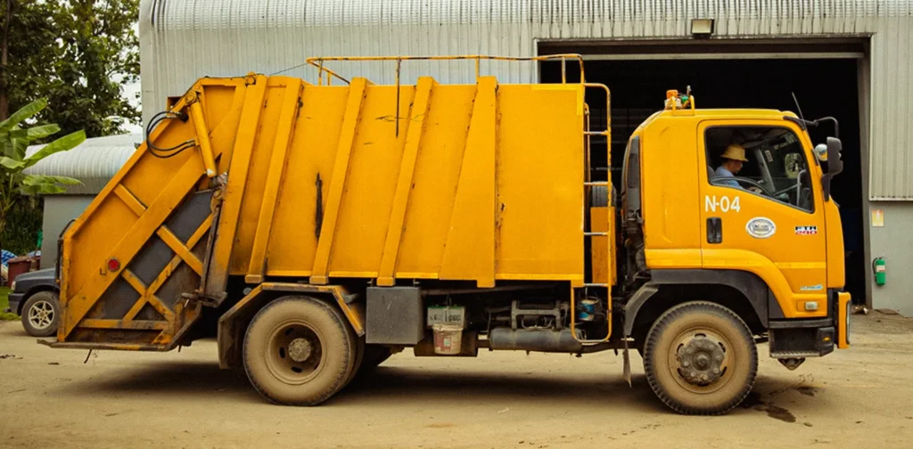 a yellow garbage track parked in front of a waste processing facility