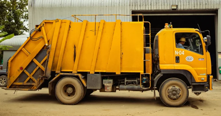 a yellow garbage track parked in front of a waste processing facility
