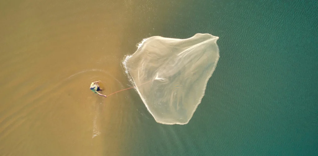 overhead shot of a fisherman spreading a fishing net at sea