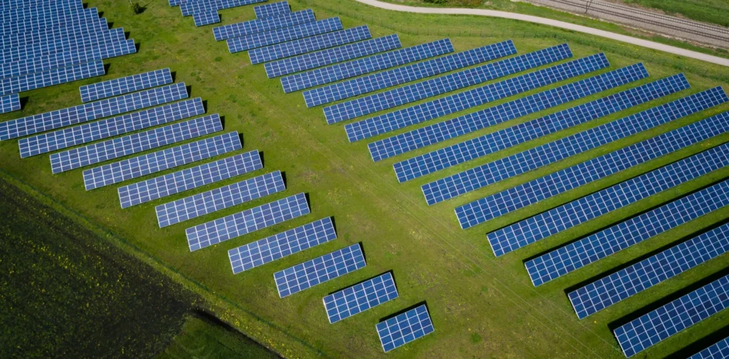 View of a large solar farm with rows of solar panels on green fields, representing the shift toward renewable energy.